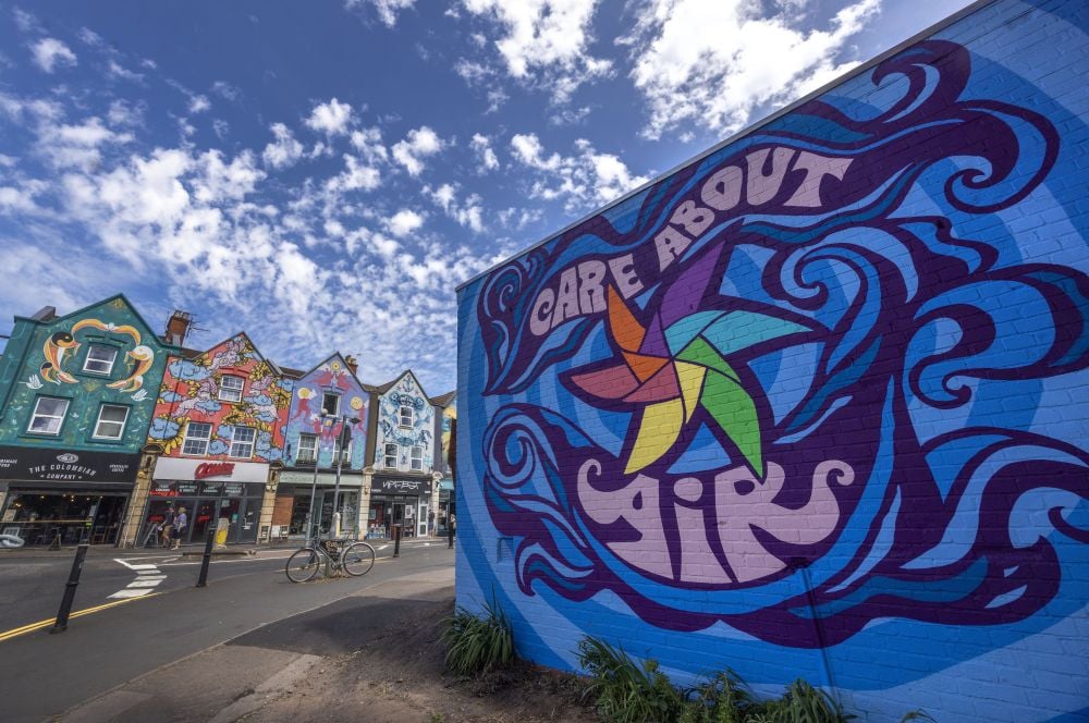 Colorful “Care About Air” mural on a blue brick wall beside a city street.